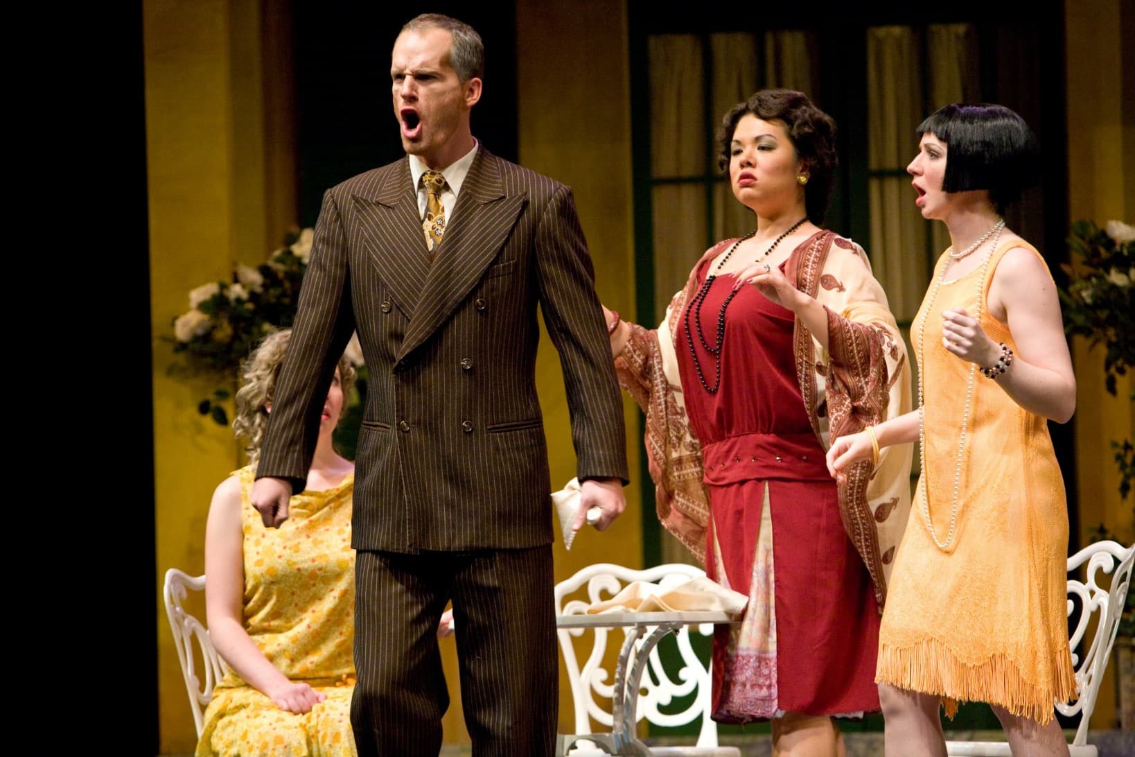 A man is singing with an assertive look on his face. An equally-assertive woman stands behind him, while a third woman is
on the side looking concerned.