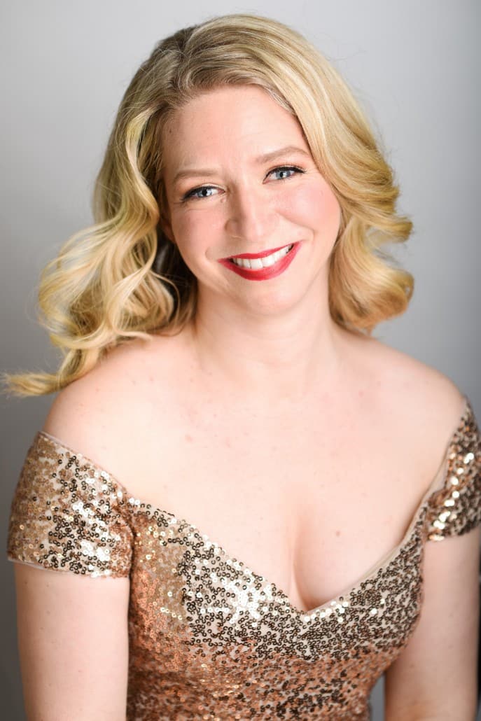 Sarah Iles wearing a golden sequins dress and smiling at the camera while sitting.