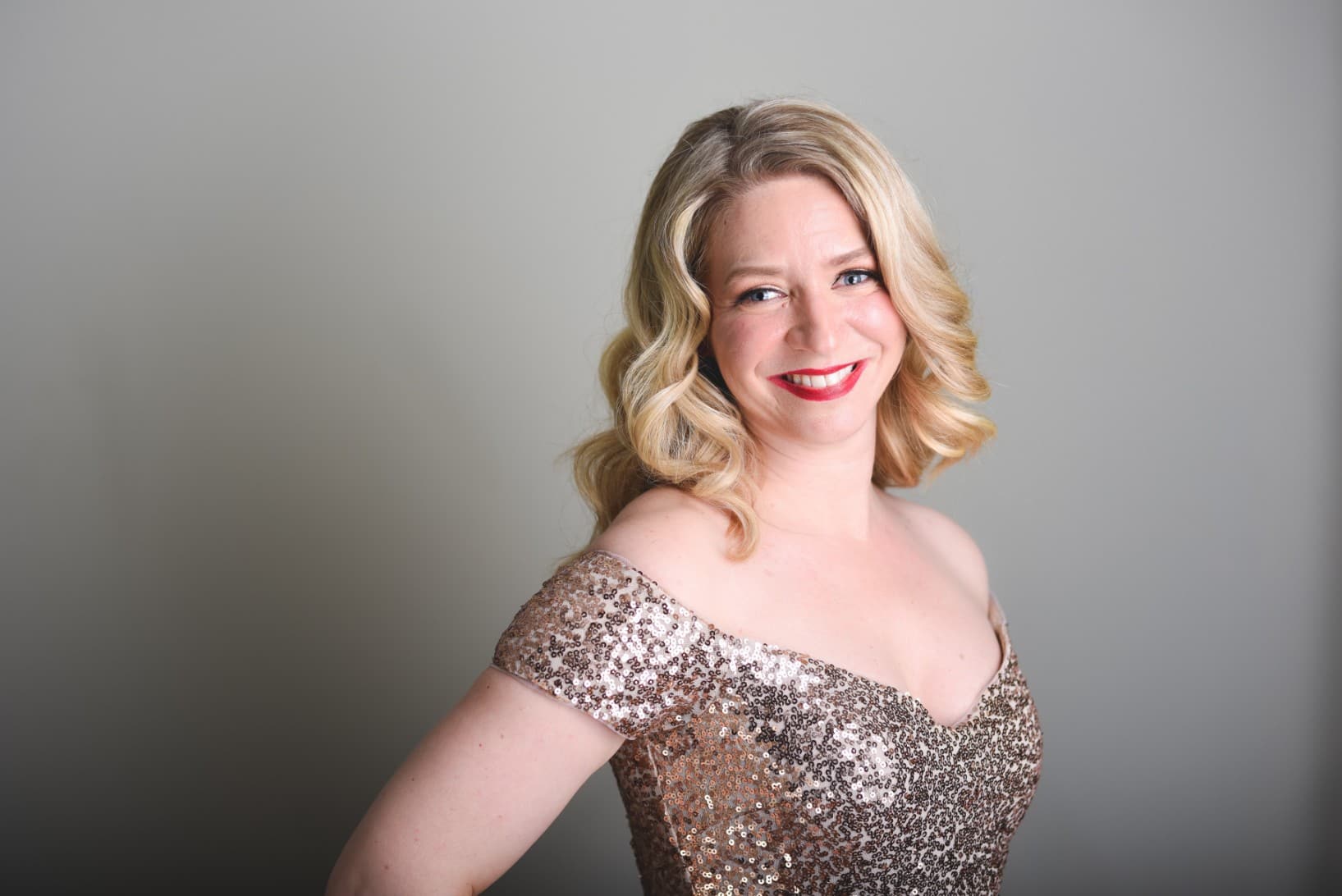 Sarah is wearing the sequins dress in this photo too, but it looks more silver than gold in this photo. She is standing,
facing slightly right, with her upper torso shifting to the center towards the camera.